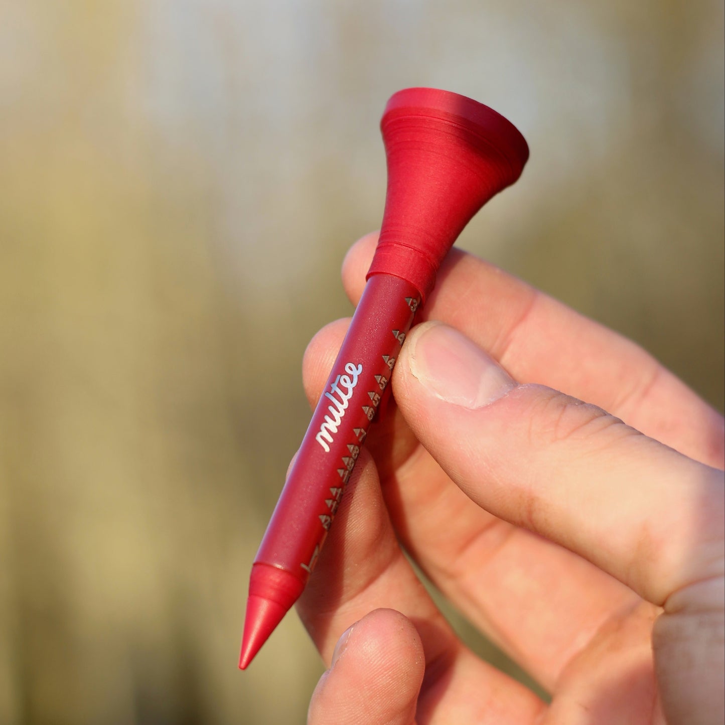 Red golf tee held in a hand with a blurred natural background